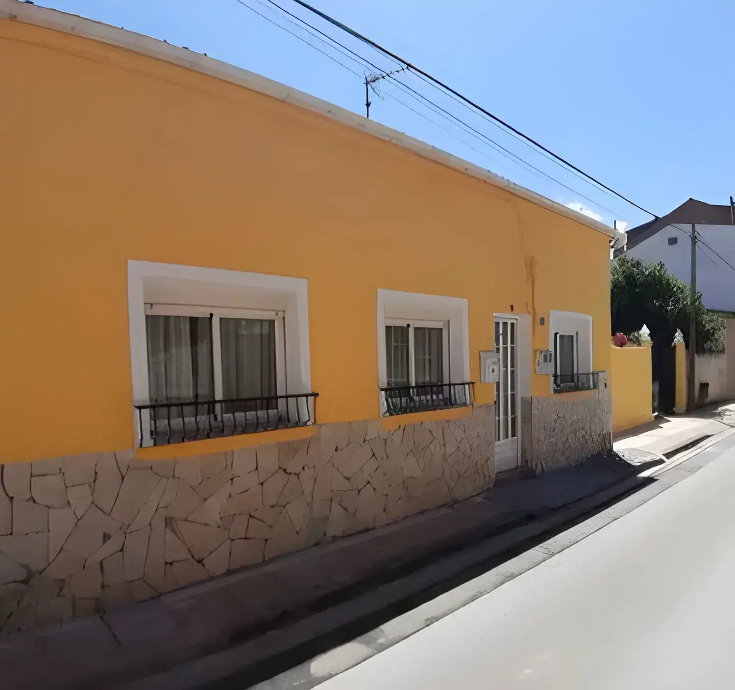 Los Pintores Móstoles Fachada de casa tradicional pintada en color amarillo con zócalo de piedra